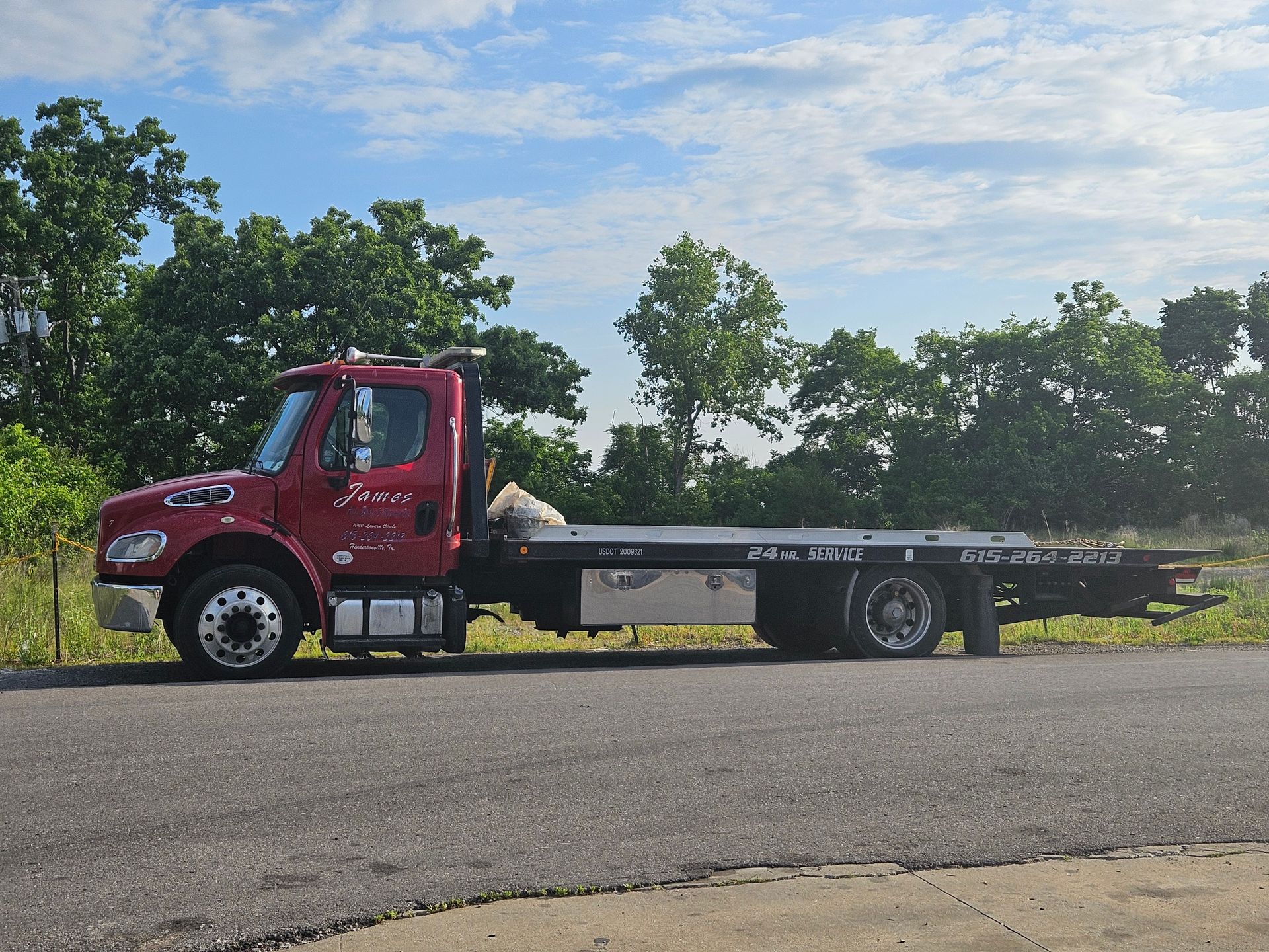 Red flatbed truck parked on a rural roadside beside trees and grass