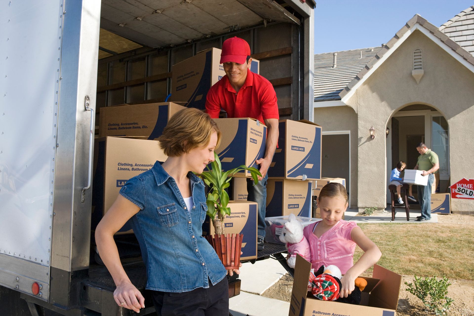 A family of four are unloading boxes from a moving truck with the help of a removalist. A family of four are unloading boxes from a moving truck with the help of a removalist.