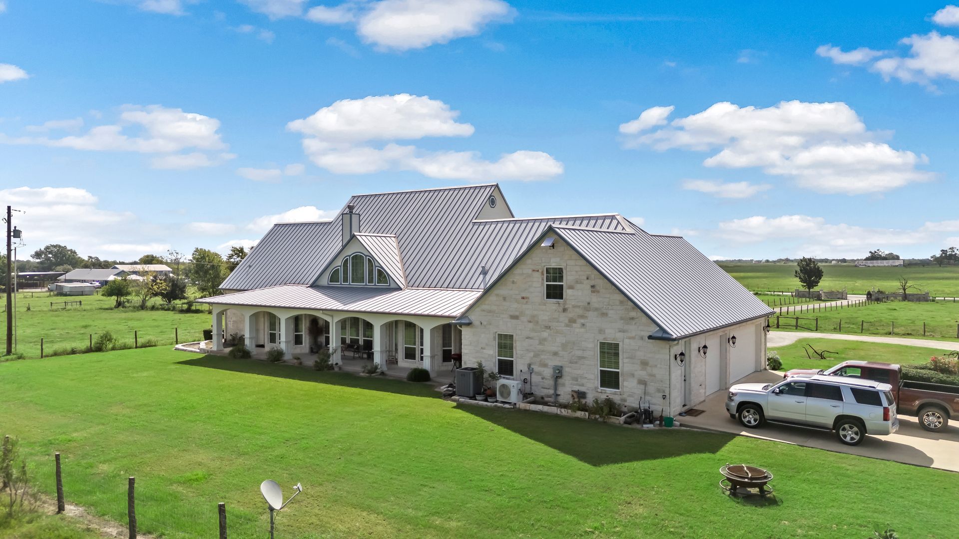 A large white house with a gray roof is sitting on top of a lush green field.