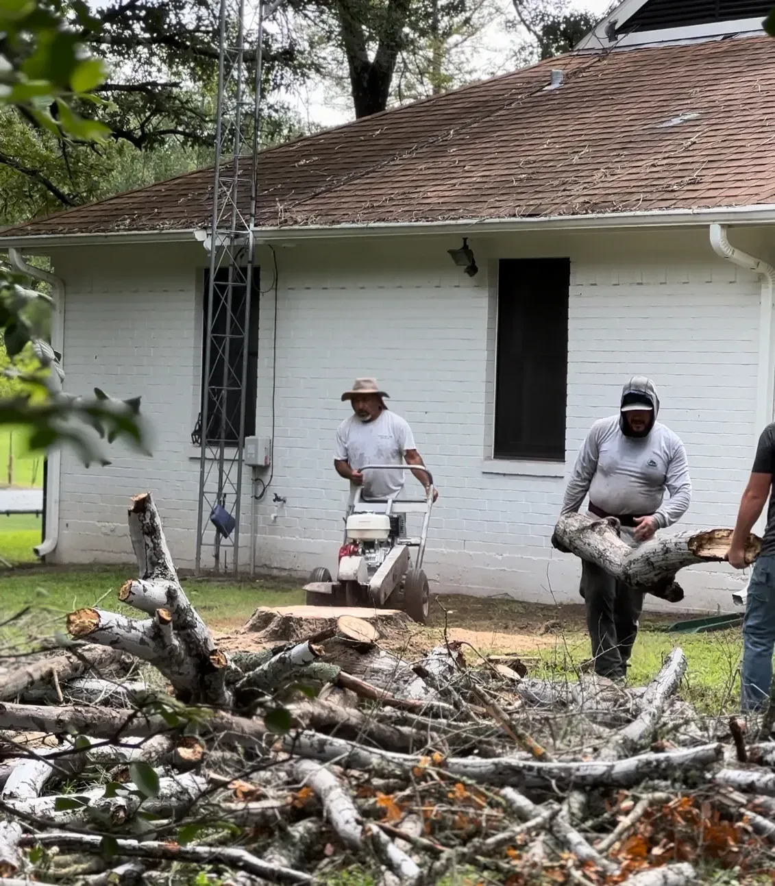 Two men are carrying logs in front of a house.
