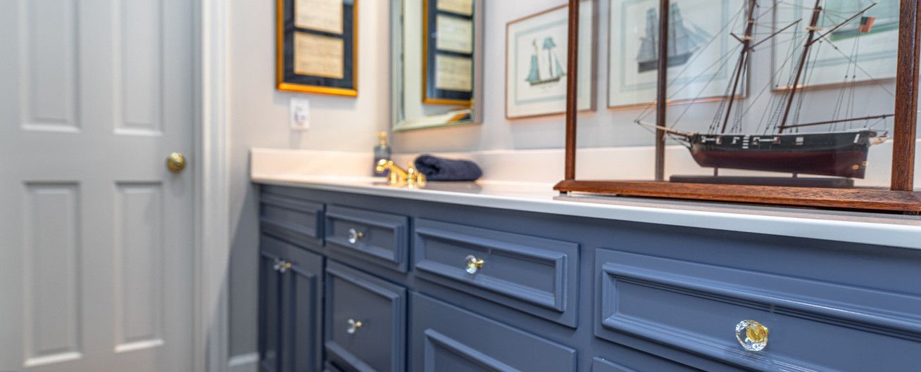 A bathroom with blue cabinets , a sink , a mirror and a model ship on the counter.