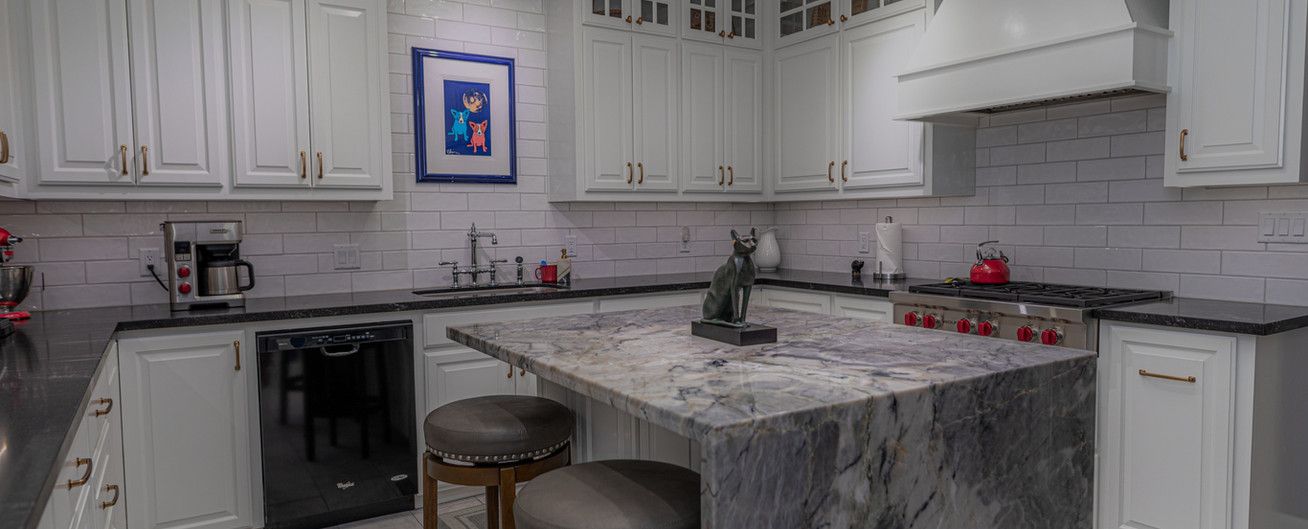 A kitchen with white cabinets , granite counter tops , black appliances and a large island.