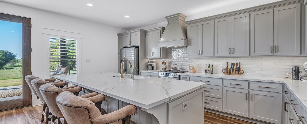 A kitchen with gray cabinets , white counter tops , and a large island.