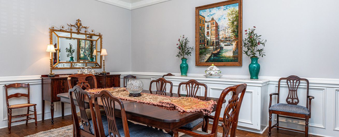 A dining room with a table and chairs and a painting on the wall.