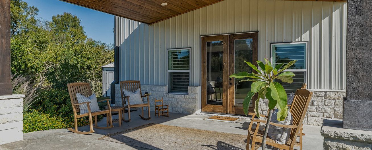A patio with chairs , a table and a plant in front of a house.