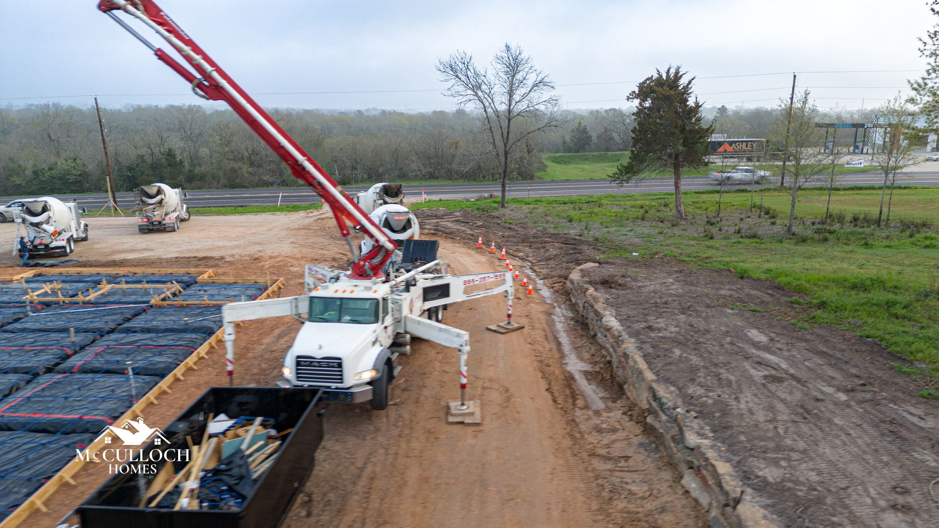 A concrete pump is being used to pour concrete on a dirt road.