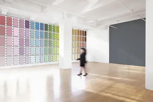 A woman is walking through an empty room with a wall of paint samples.