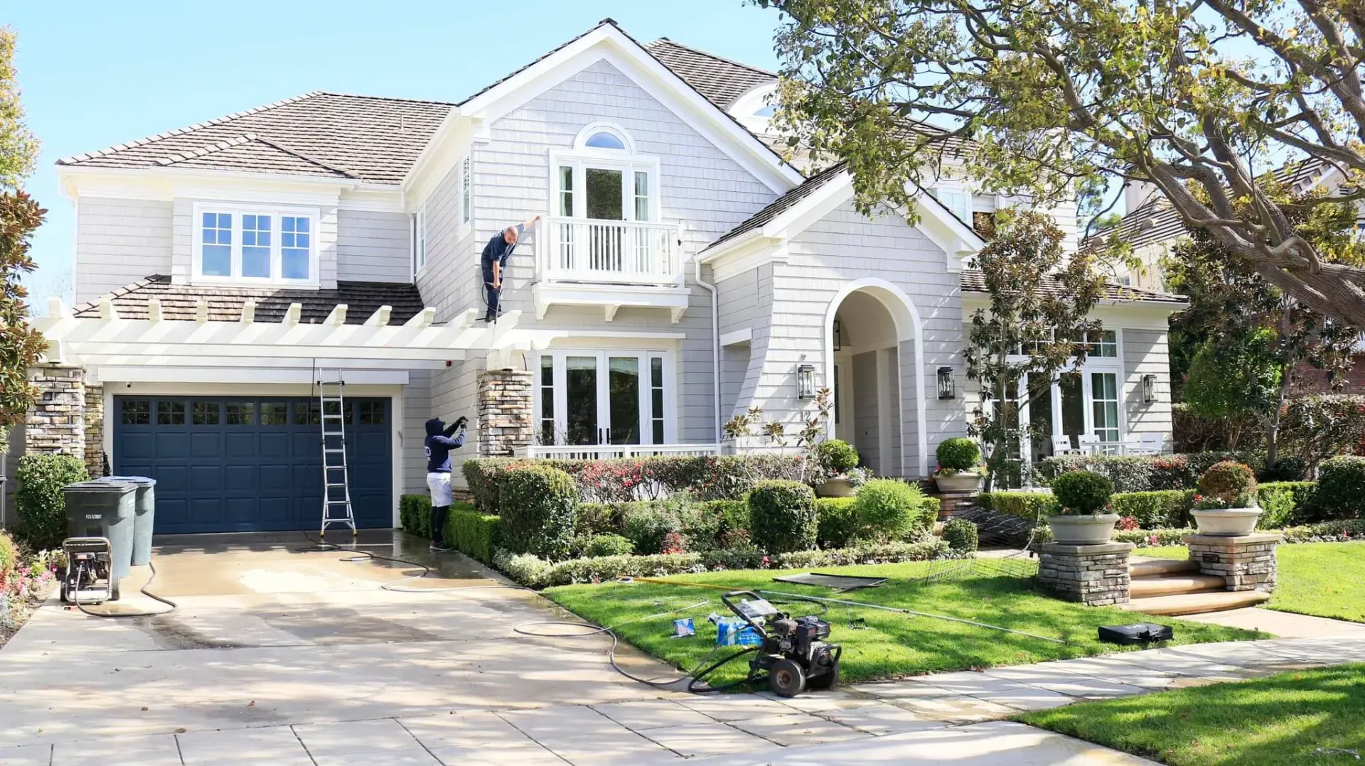 A large white house with a blue garage door is being painted.
