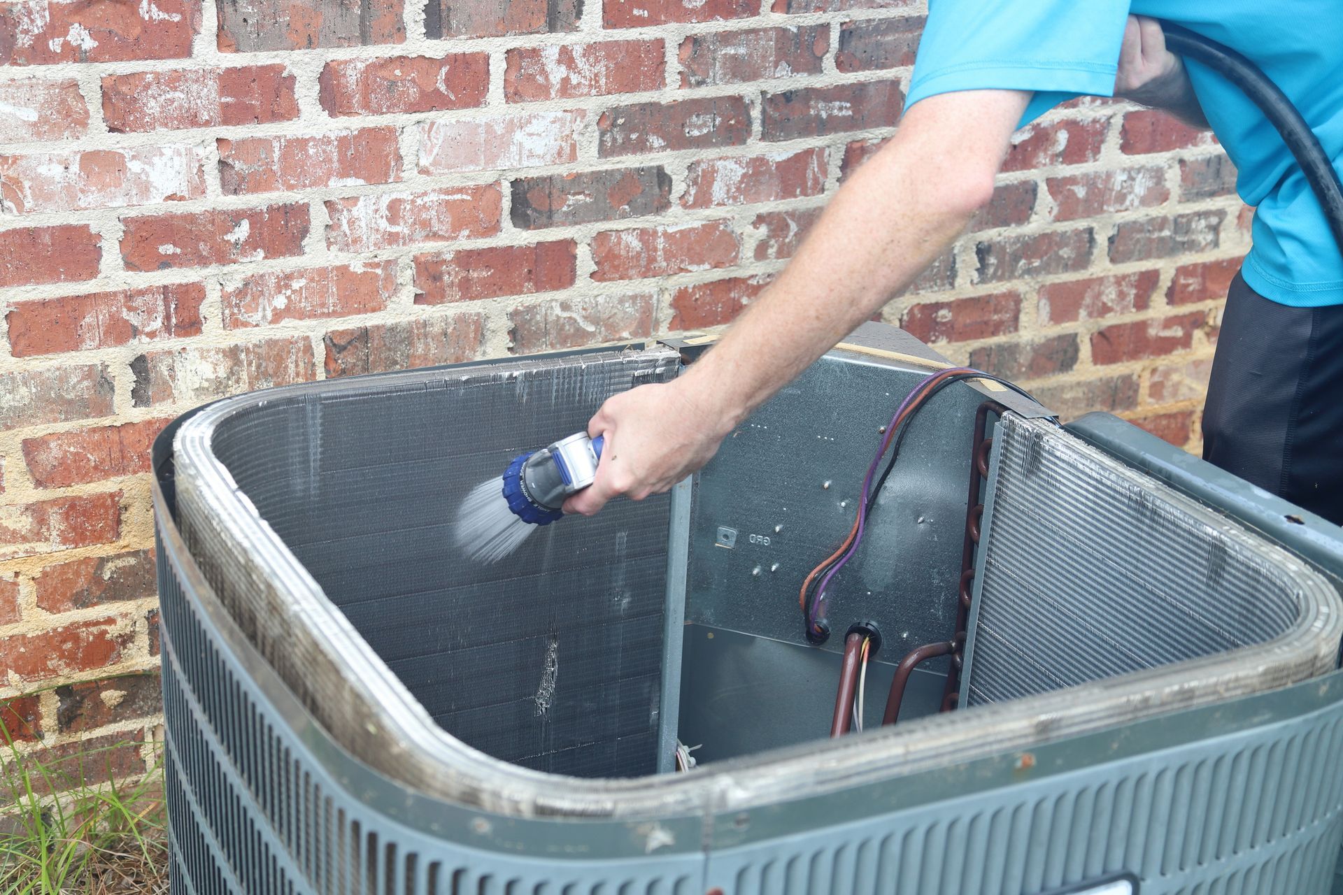 Person cleaning an air conditioning unit with a hose near a brick wall. Person cleaning an air conditioning unit with a hose near a brick wall.