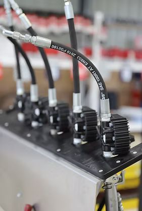Black hydraulic hoses connected to a metal plate with a series of components; industrial setting.