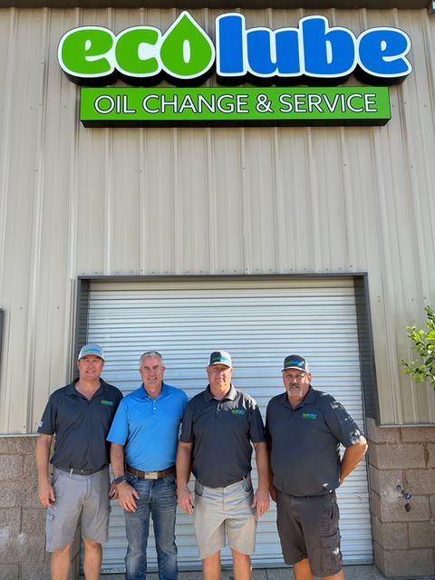 Four men standing in front of an EcoLube oil change and service building. They are wearing caps and company shirts.