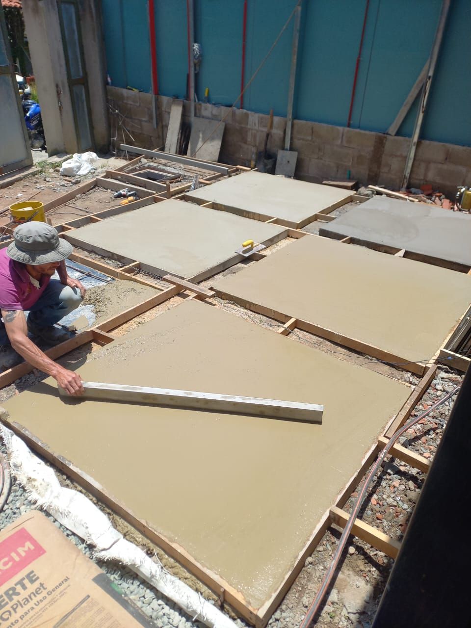 Obrero alisando losas de hormigón fresco en una obra con una llana larga.