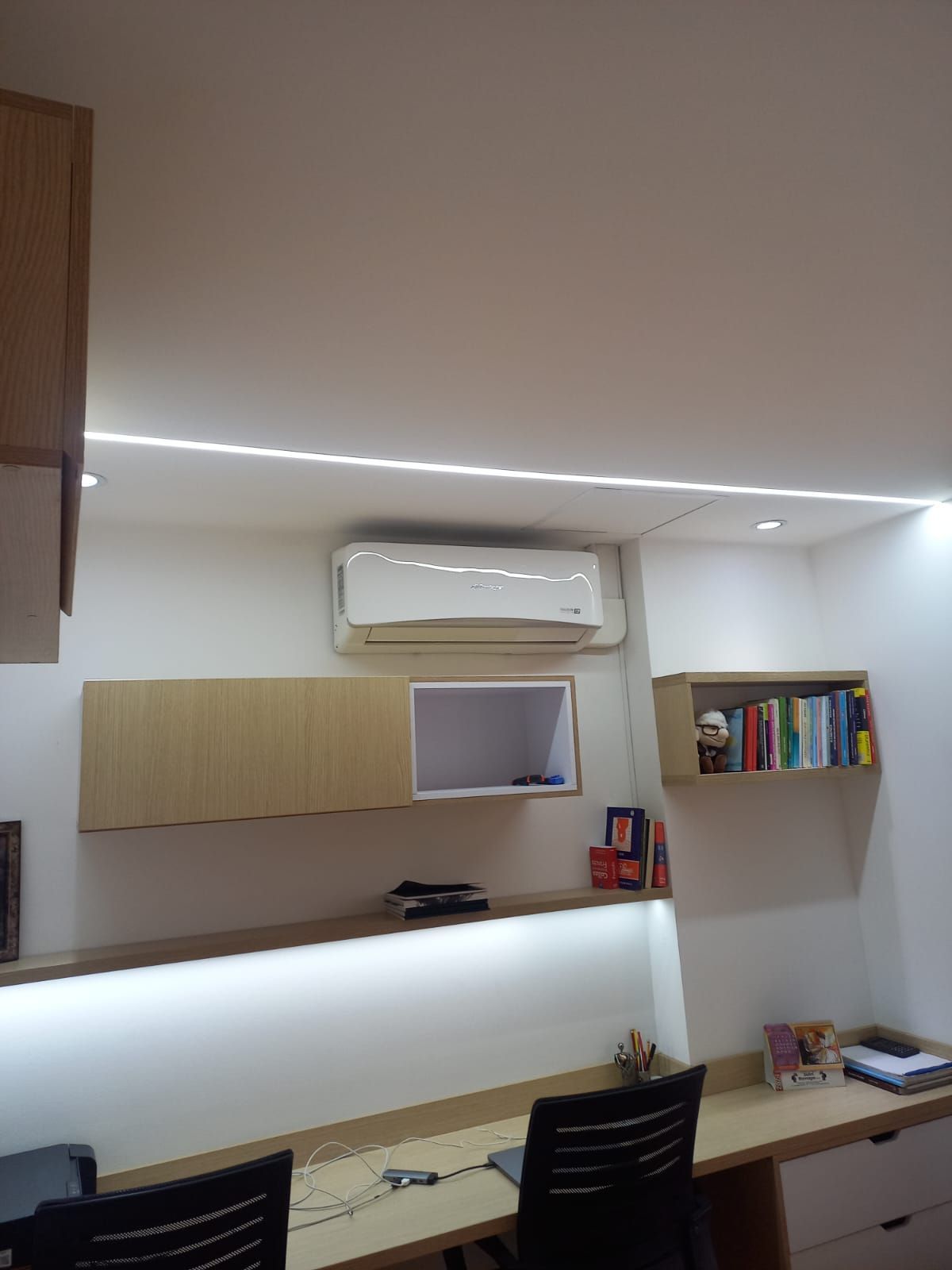Oficina moderna en casa con estantes blancos, escritorio, silla negra, aire acondicionado mural y librerías.