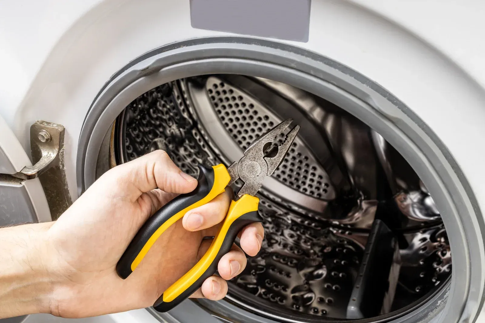 Hand using pliers to remove debris from a washing machine drum