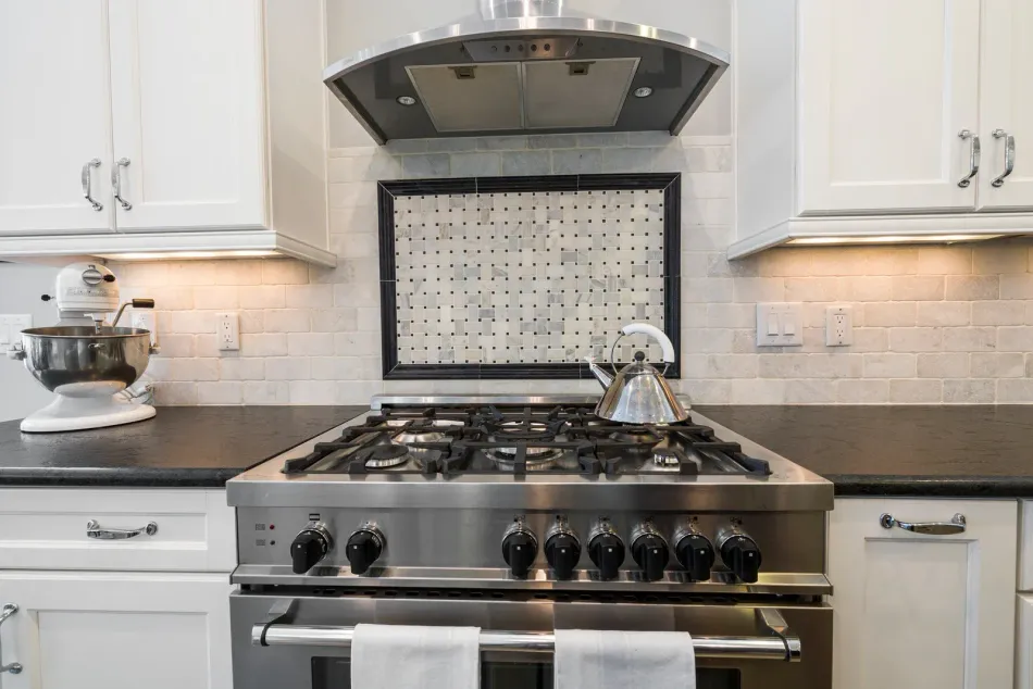Modern kitchen with stainless steel gas range, white cabinets, and mosaic tile backsplash