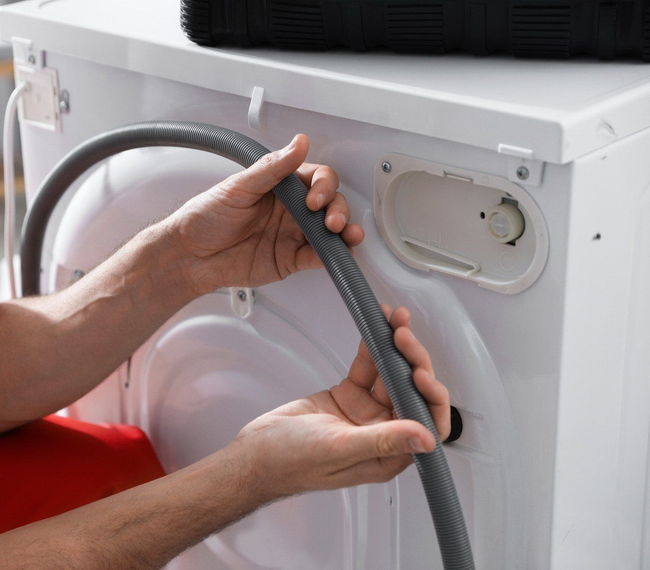 Hands threading a gray dryer vent hose into the back of a white appliance.