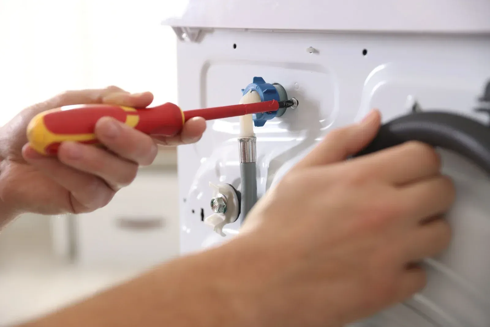 Hands using a screwdriver to repair a white appliance panel with a black hose attached