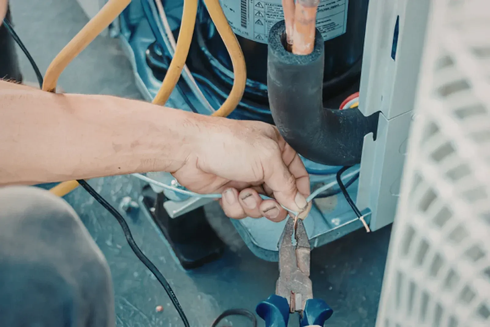 Hand using pliers to cut a wire inside a machine cabinet with blue cables.