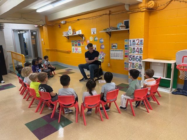 Sean Noble reading his book Tula the Toothfairy to a group of preschool children in a classroom