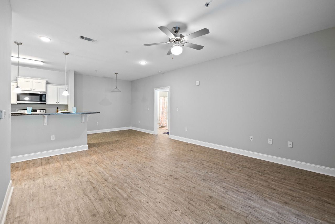 Open-concept living area with kitchen bar, ceiling fan, and wood-look flooring.