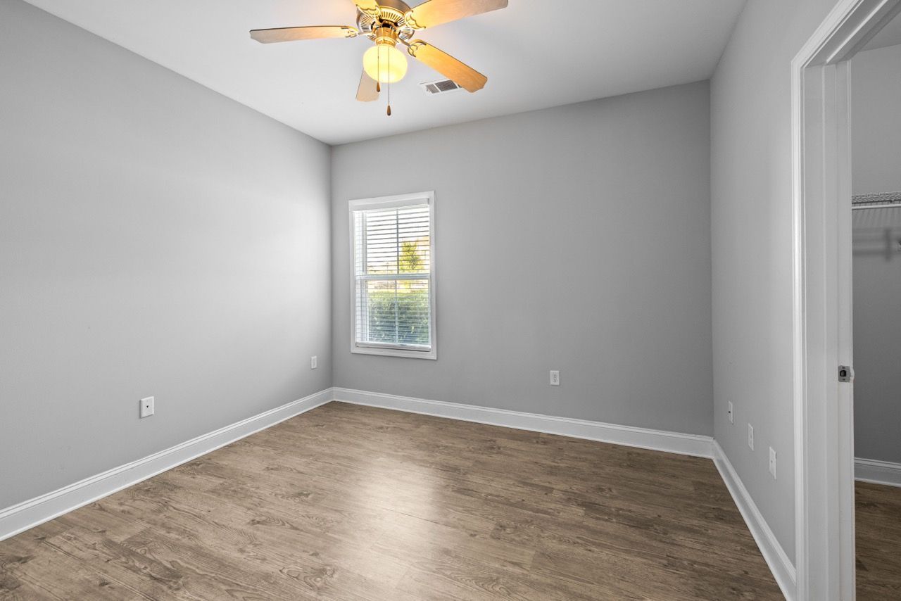 Empty bedroom with gray walls, a window, ceiling fan, and open closet.