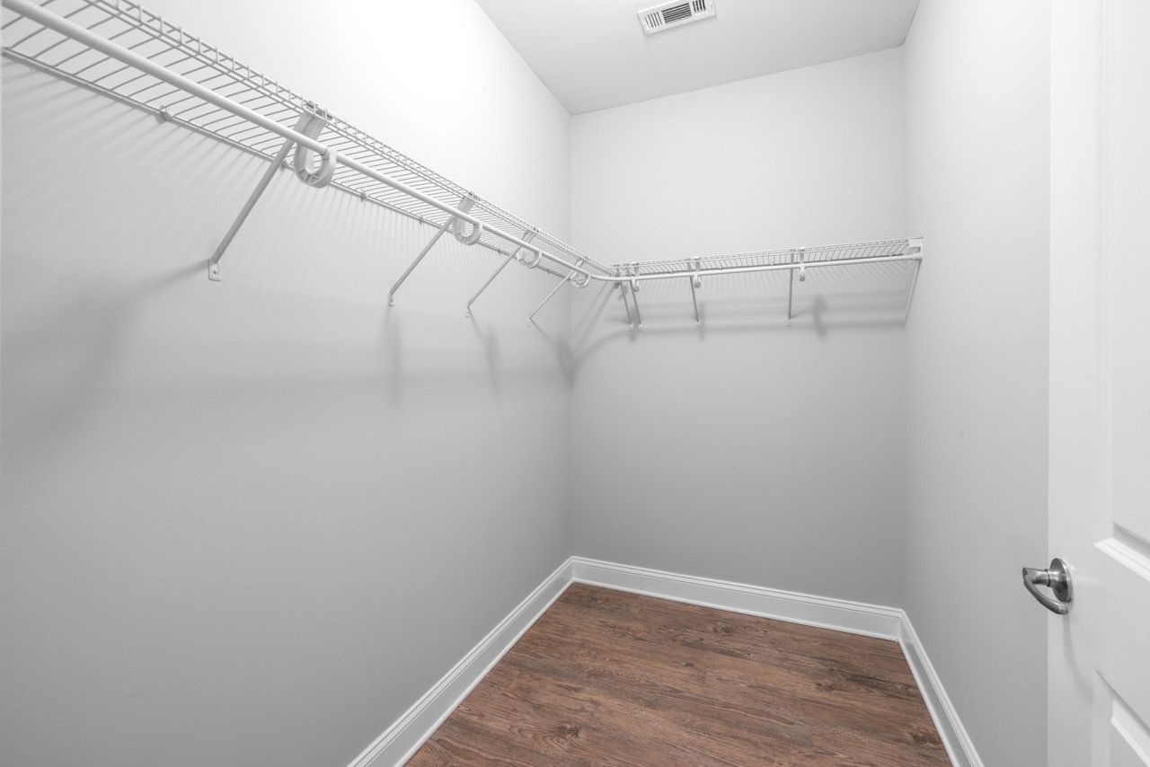 Walk-in closet with white wire shelving along two walls and wood flooring.