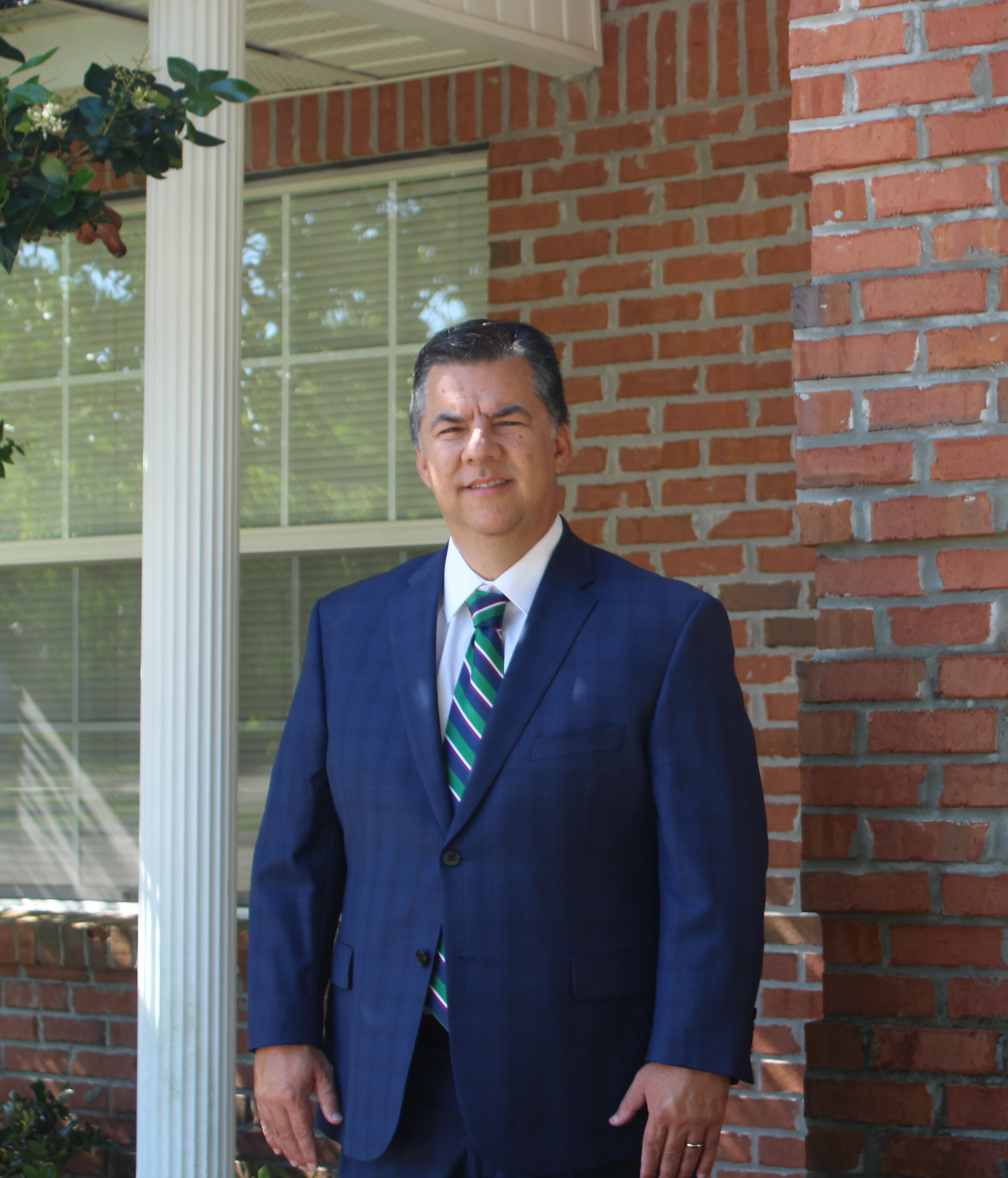Man in a navy suit standing by a brick wall and column outside a building
