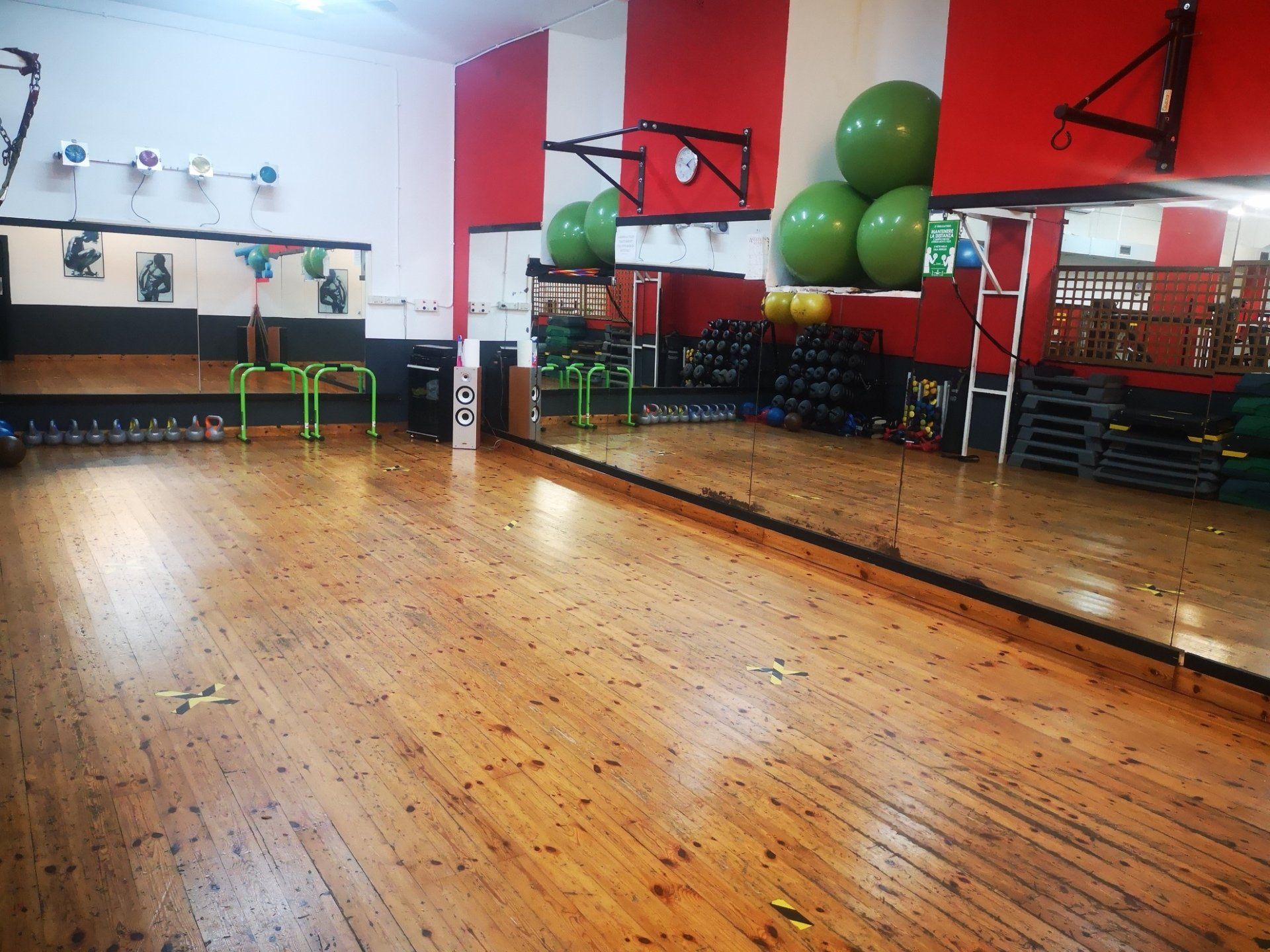 Interno di una palestra con pavimento in legno, specchi, attrezzi ginnici e pareti rosse e bianche.