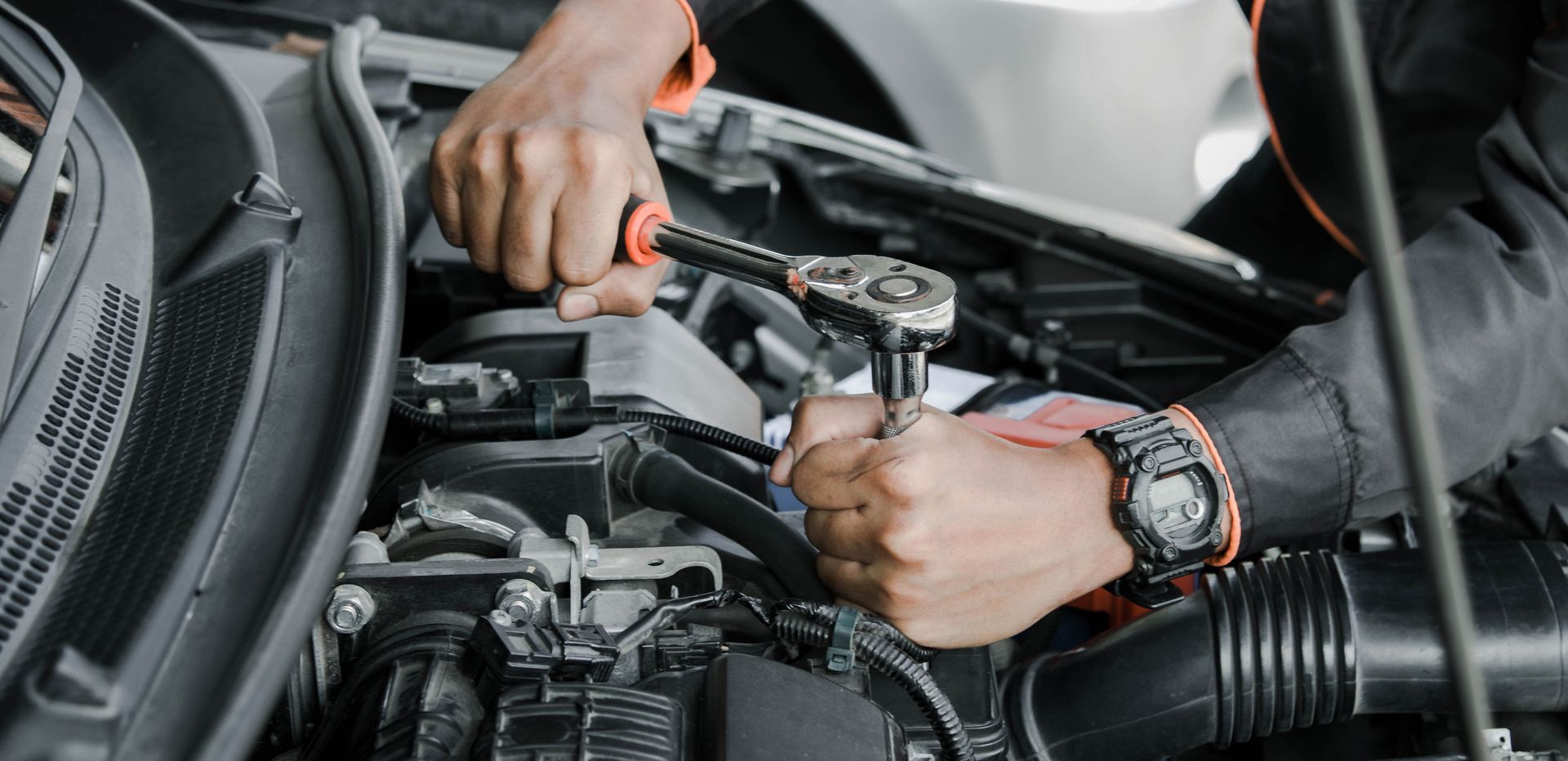 A man is working on the engine of a car with a wrench.