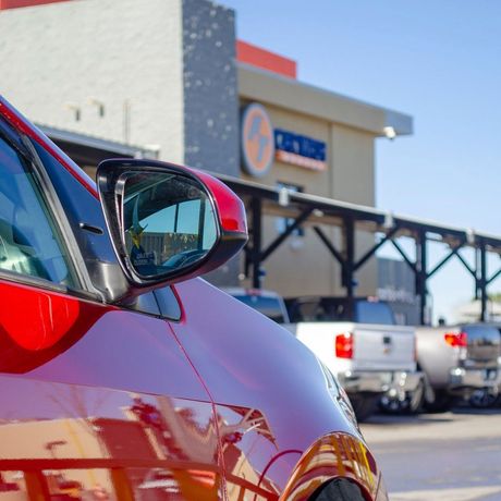 Red car parked outside a store with pickup trucks in the background