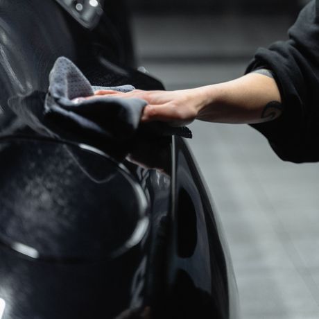 Hand brushing a black car’s glossy body near the wheel in a garage