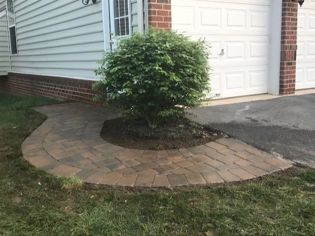 Paver walkway curves around a shrub, in front of a white garage door.