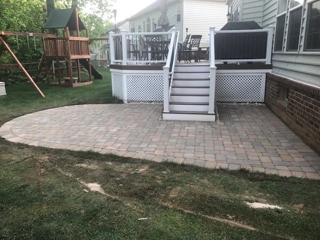 Brick patio in backyard, leading to raised deck with stairs and playground in background.
