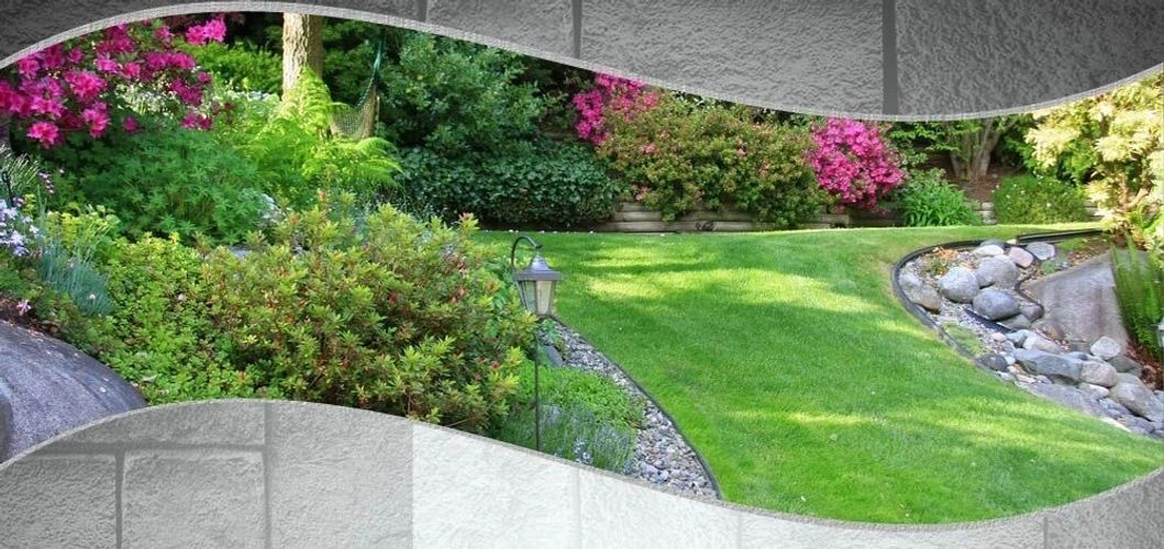 Lush garden with green lawn, shrubs, and pink flowers, bordered by a stone wall.