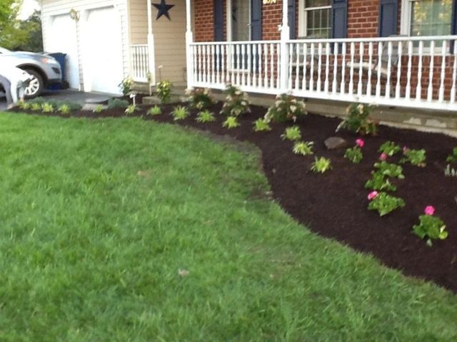 Front yard with freshly mulched flower beds and pink flowers beside a brick house porch