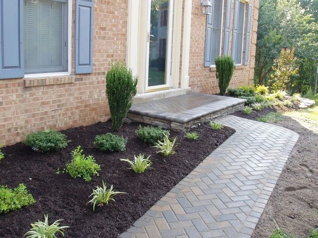Front entrance of a brick house with a stone walkway and mulched landscaping with small shrubs