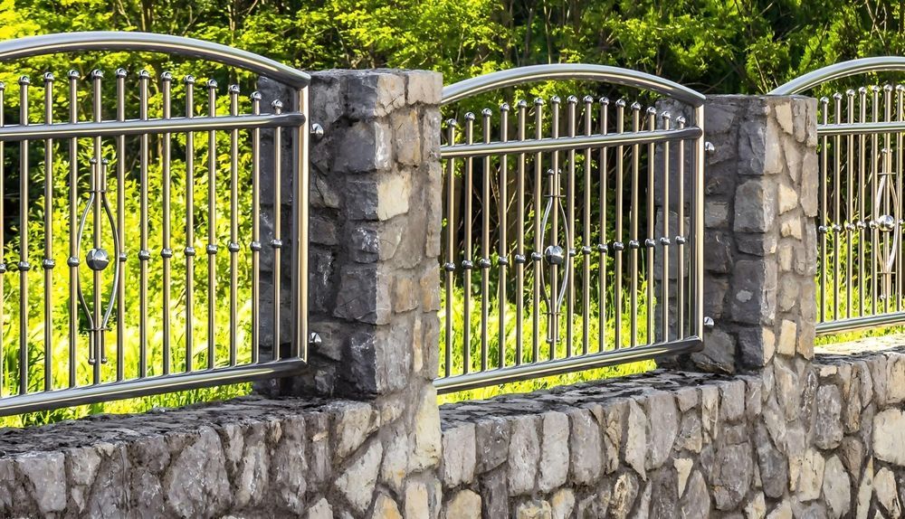 Stone wall with metal gates and a green garden behind them in sunlight