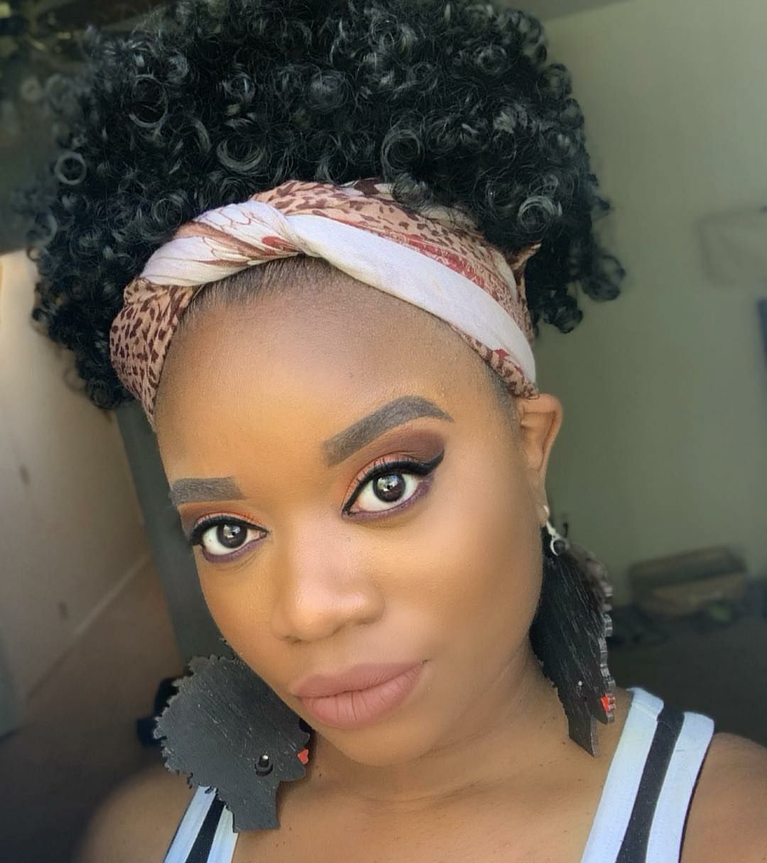 A person with curly hair and a patterned headband, wearing dark statement earrings, gazes at the camera.