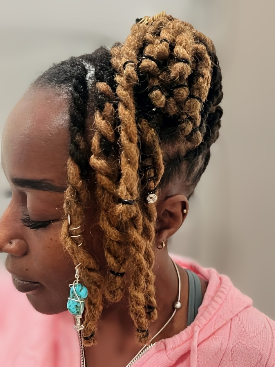 A person with two-tone brown and black twisted hair styled in a high bun with some pieces framing the face.