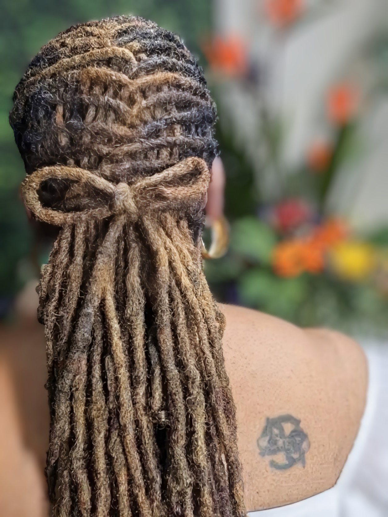 Back view of long brown dreadlocks styled in a half-up ponytail featuring a bow made from the hair.