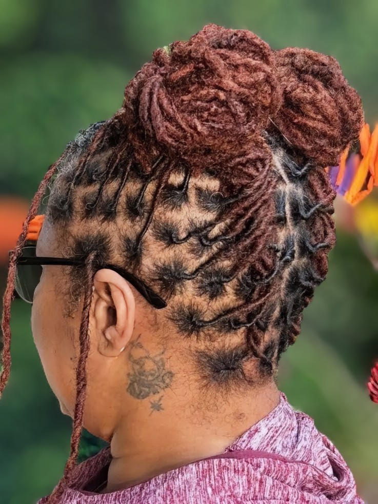 A person with auburn locs styled in two high buns, featuring a grid-patterned scalp sectioning.