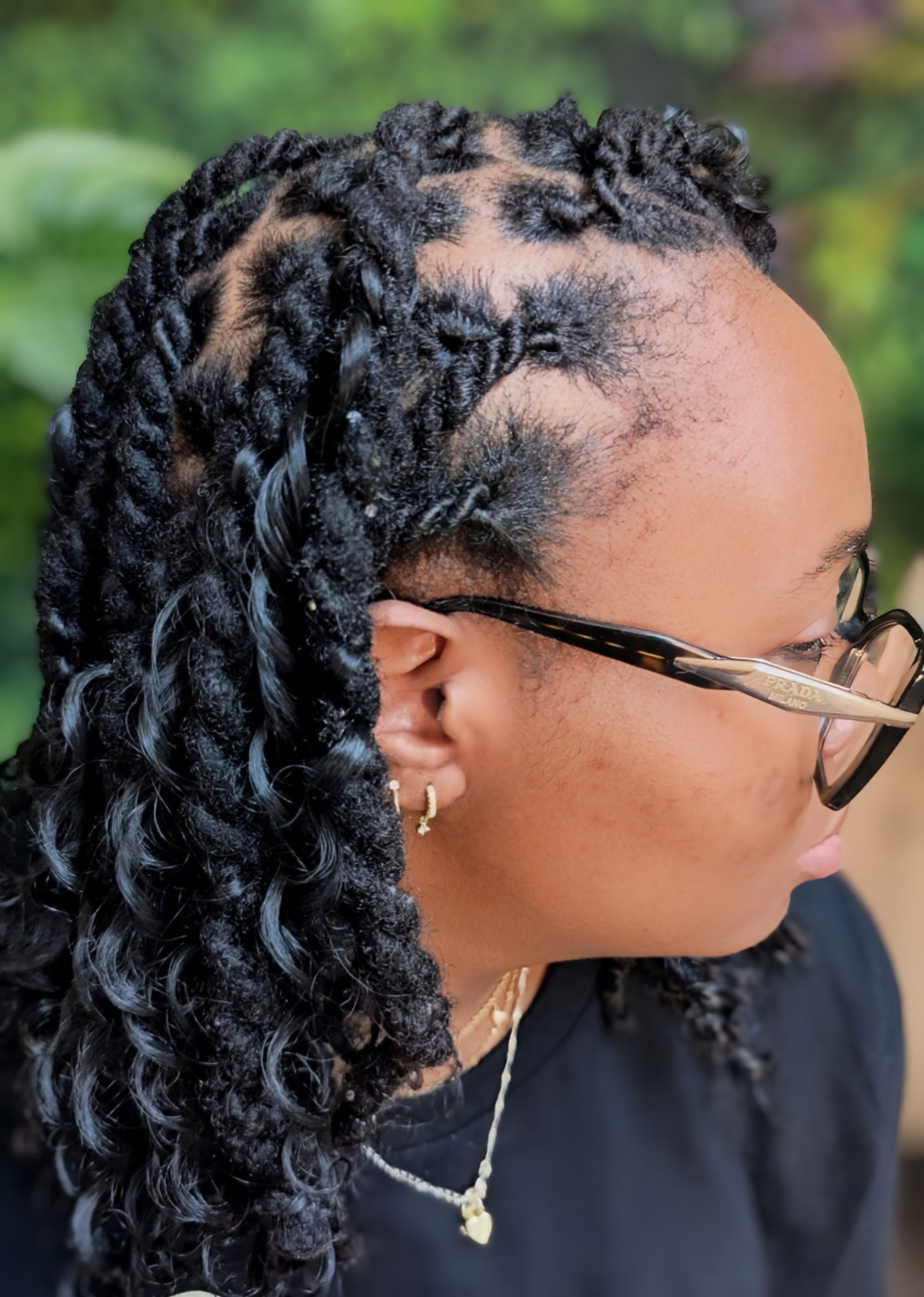 A side view of a person with dark, shoulder-length twists, with hair parted into box sections and secured with small bands.