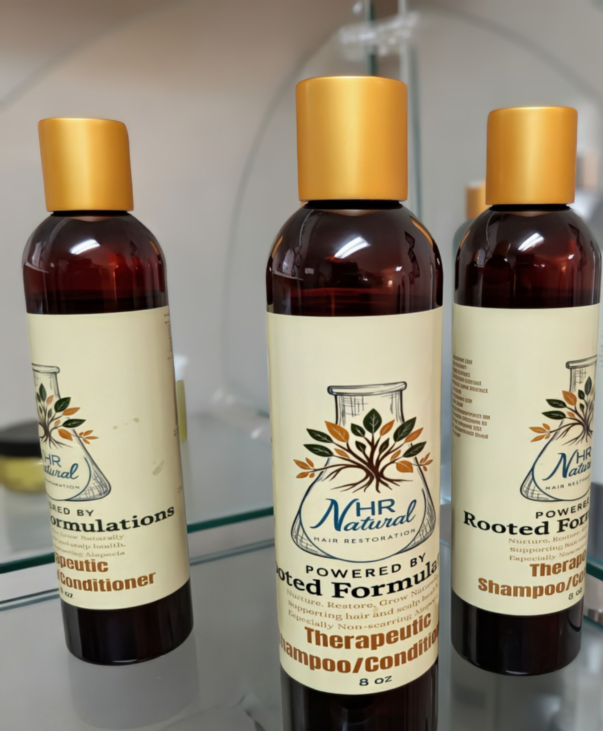Three bottles of NHR Natural therapeutic shampoo/conditioner with brown plastic containers and gold caps on a glass shelf.