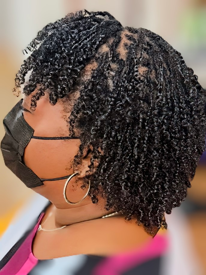 Side profile of a person wearing a black face mask, showcasing short, dark, textured curly hair.