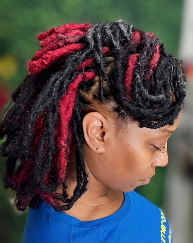 A side view of a person with shoulder-length, textured locs styled in a blend of black and deep red colors.