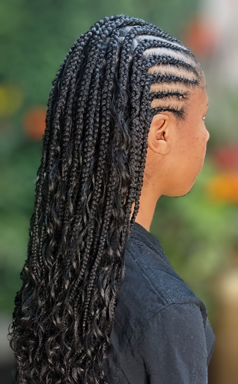 A side view of a person with long, black hair styled in neat cornrows that transition into loose, flowing waves.