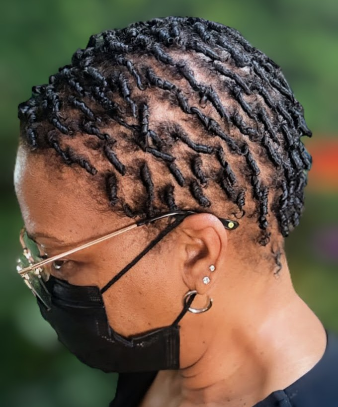 A person wearing glasses and a black face mask, showcasing a short, textured hairstyle with defined, coiled strands.