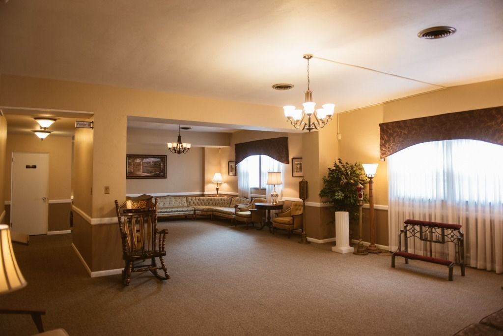 Spacious beige living room with carpet, chairs, chandelier, piano, and large curtained windows