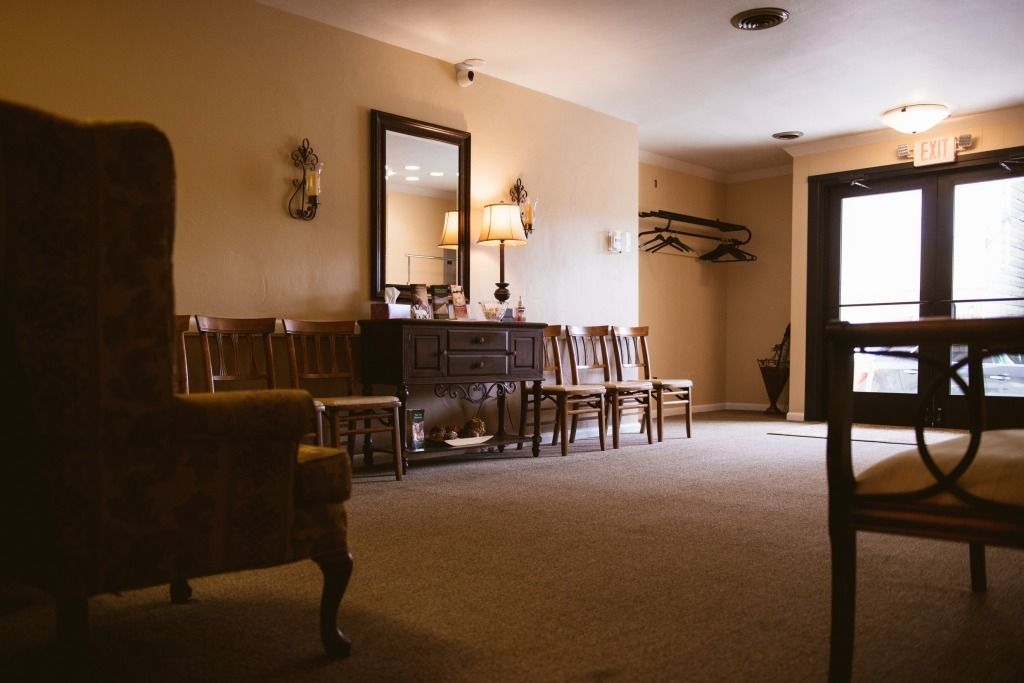 Dimly lit dining room with wooden chairs, a mirror, and a table near a bright window