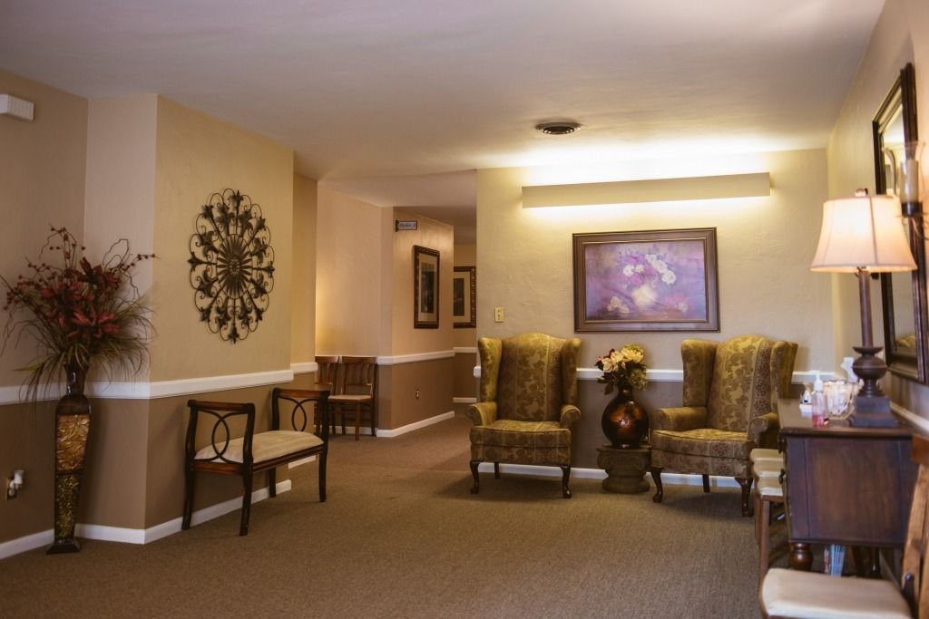 Warm hotel lobby with beige walls, armchairs, lamp, side table, and framed artwork.